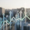 9/18 ソフト９９コーポレーション株急騰の理由を解説。株価の急騰を象徴する抽象的な矢印やグラフを背景に、都市の風景がぼかされています。