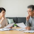 定年後の保険見直しによる家計への影響を考える様子を描いたイメージ。落ち着いた室内で、年配の夫婦が保険の書類を見直すシーン。