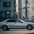 クルマ高騰時代の車両保険完全ガイドをテーマにした日常的な日本の都市風景。人々の生活の中で考慮される車両価格の影響が感じられるシーン。