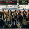 推し活遠征のキャンセルリスクに対応する推し活キャンセル保険の意義を示す、駅で旅行準備をするファンたちの姿。