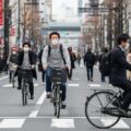 自転車の青切符導入による反則金1万2000円と保険料値上げについて、都市の日常風景を描写した画像です。