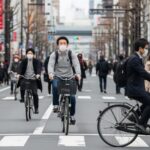 自転車の青切符導入による反則金1万2000円と保険料値上げについて、都市の日常風景を描写した画像です。