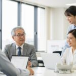 再雇用時の社会保険に関するガイド。オフィスでの仕事をするシニアと若手社員の交流を描写した画像。